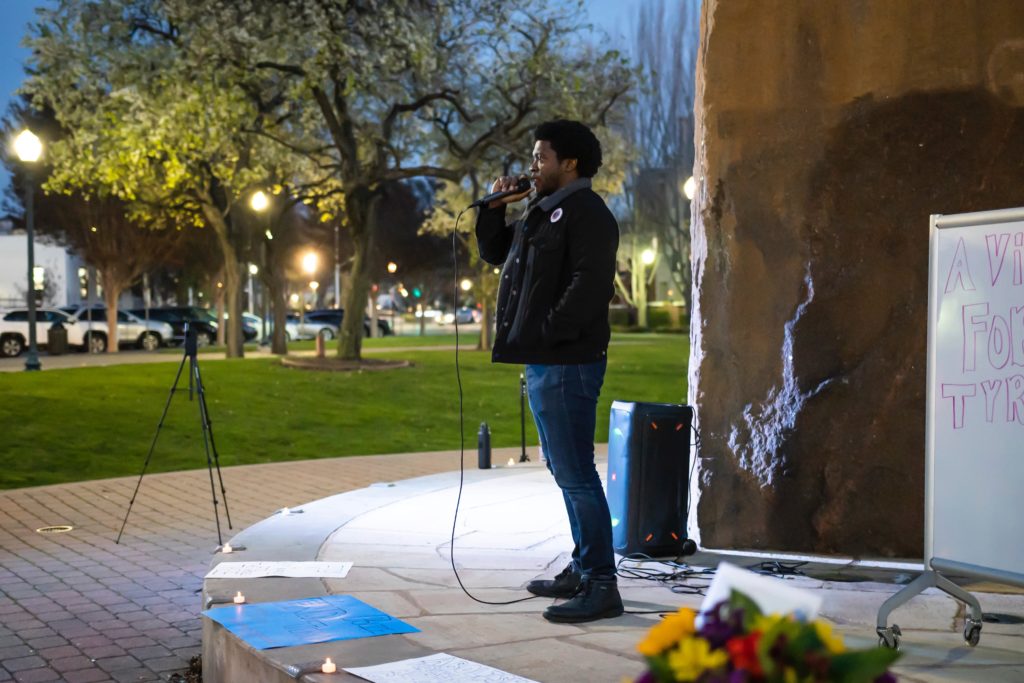 One organizer on stage in front of City Hall speaking while other organizers and audience members listen.