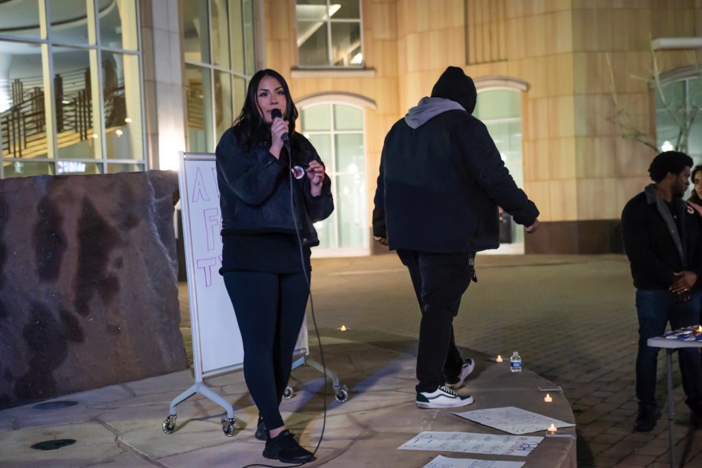 One organizer on stage in front of City Hall speaking while other organizers and audience members listen.