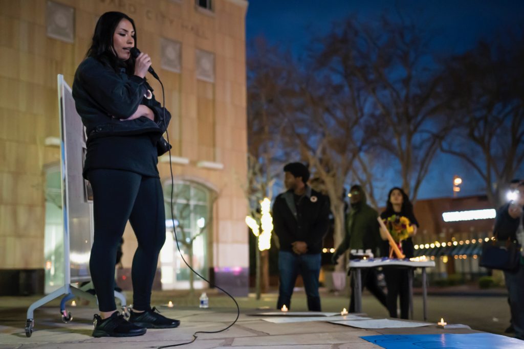 One organizer on stage in front of City Hall speaking while other organizers and audience members listen.