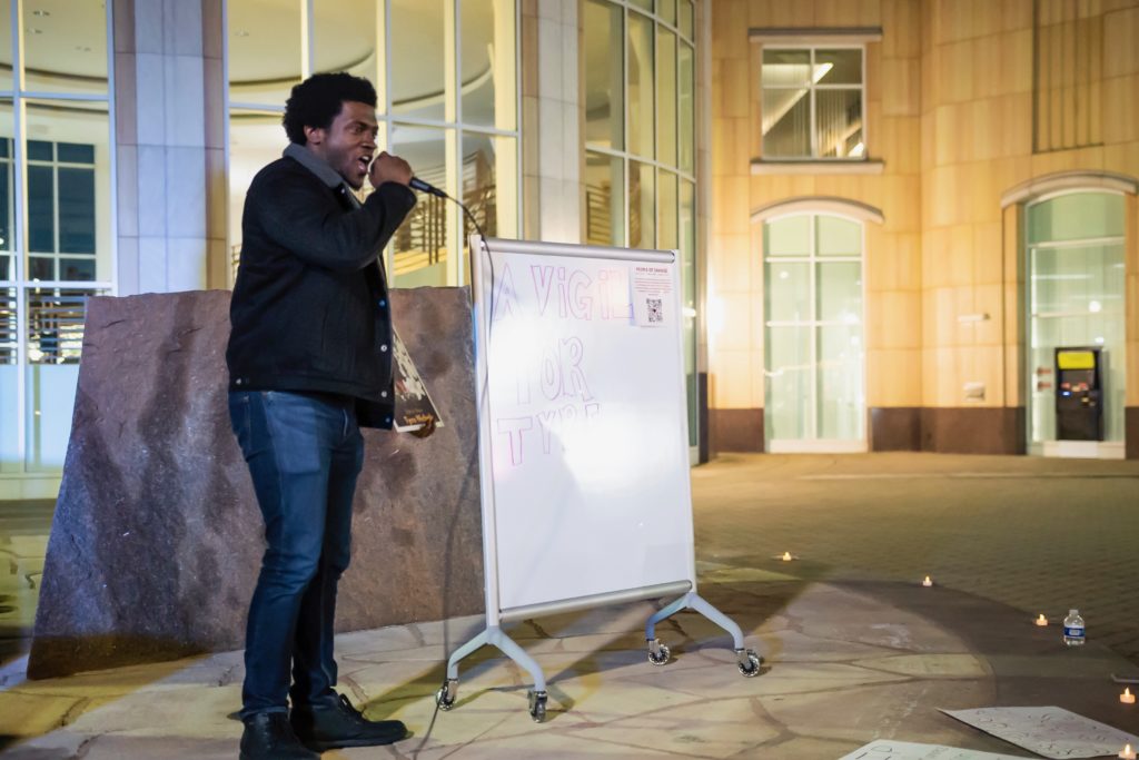 A man stands on stage speaking passionately about bringing change to an audience at night in front of city hall.