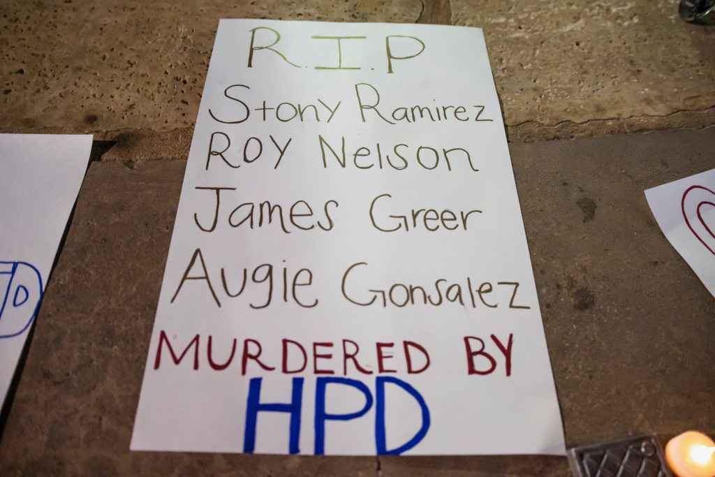 A protest sign that reads "r.i.p., Stony Ramirez, Roy Nelson, James Greer, Augie Gonsalez Murdered by HPD.