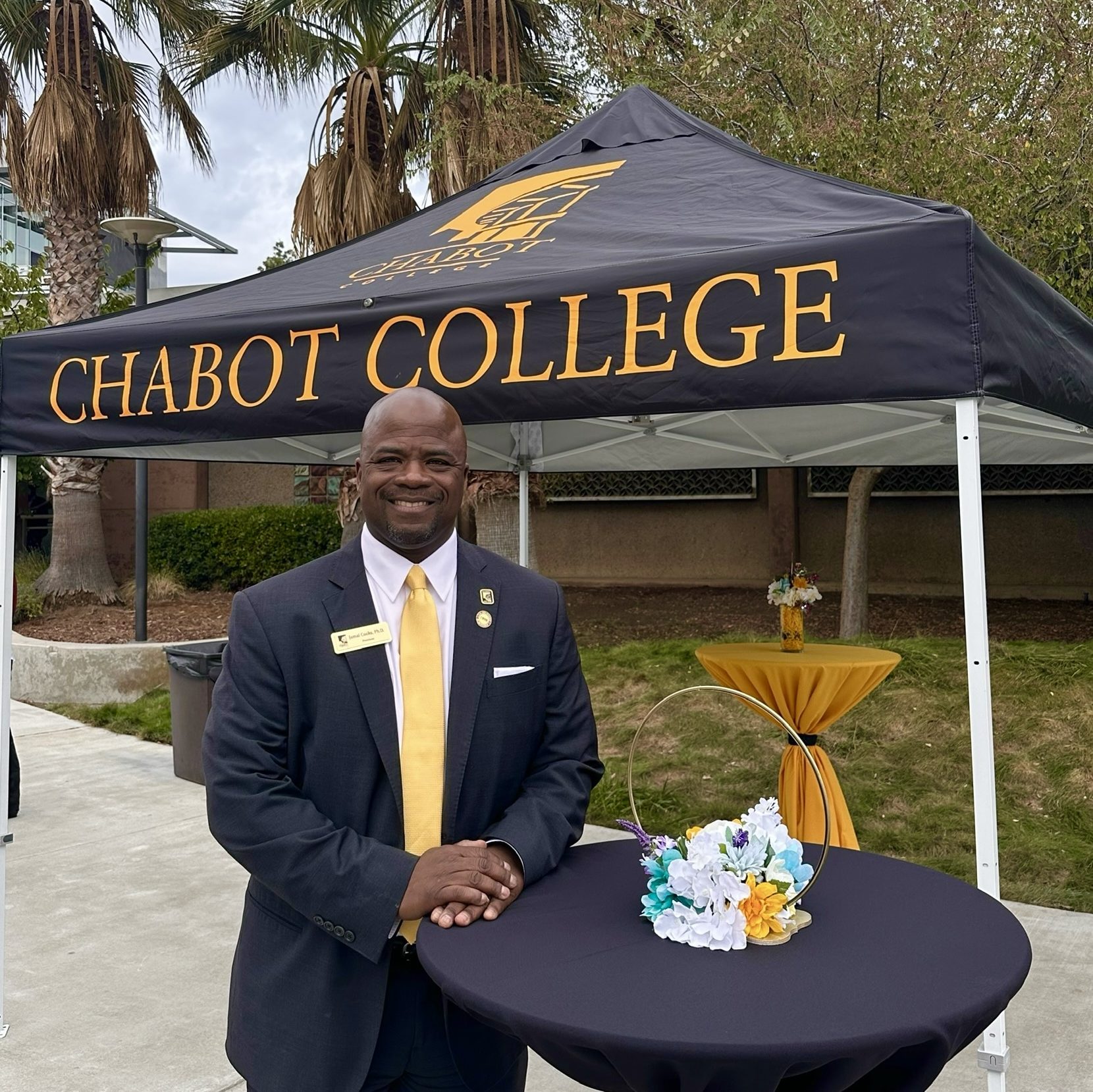 President Jamal Cooks at his welcome reception in suit and tie under tent with a Chabot College logo. 