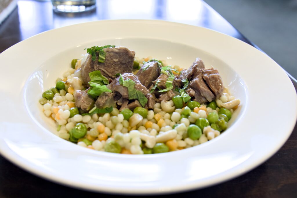 Pieces of lamb sit on top of a bed of peas and corn in a bowl.