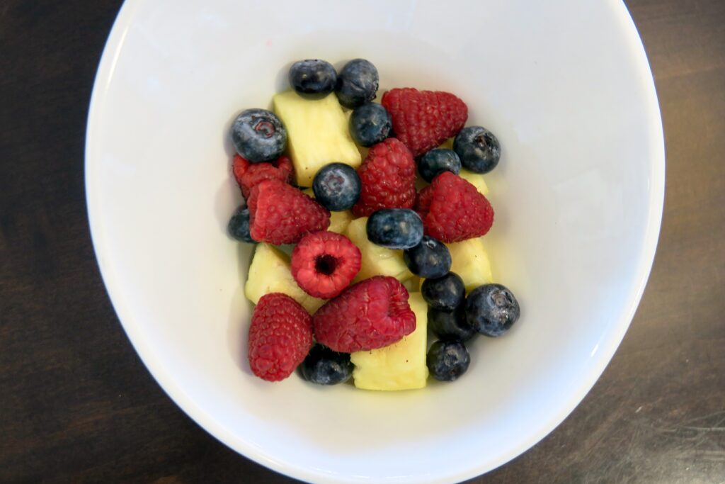 A bowl filled with pineapples, raspberries, and blueberries